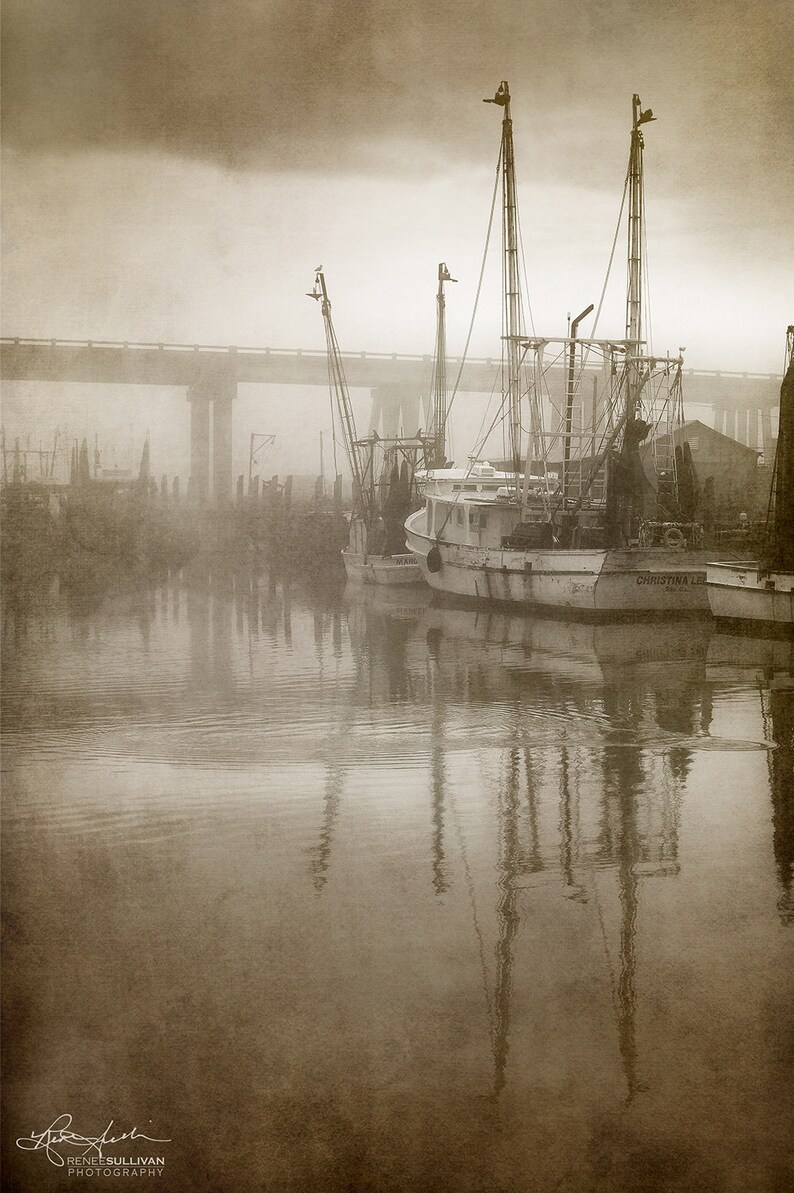 May include: A sepia-toned photograph of three fishing boats docked at a pier in a foggy harbor. The boats are silhouetted against the fog, and the water is calm and reflective. The name of the boat in the foreground is "CHRISTINA L."