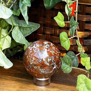 May include: A red, white, and brown agate sphere on a clear acrylic stand. The sphere is polished and has a swirling pattern.