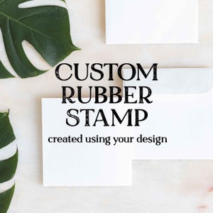 May include: White square cards and envelopes with the text "CUSTOM RUBBER STAMP" and "created using your design" in black. Green leaves are in the background. The image suggests custom stationery.