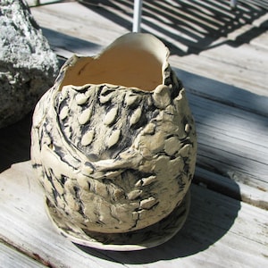 May include: A white ceramic planter with a textured, black and white design. The planter has a wide, round opening and a slightly curved base.