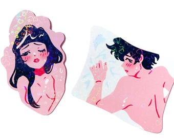 Puede incluir: Dos pegatinas holográficas rosas con ilustraciones de una mujer y un hombre. La mujer tiene el pelo largo y negro y lleva un collar rojo. El hombre tiene el pelo corto y negro y está sin camisa. Ambas pegatinas tienen un fondo blanco con un patrón de corazones.