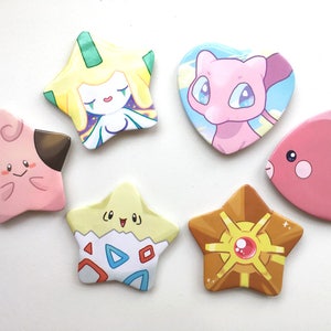 May include: Six colorful star-shaped and heart-shaped pins featuring cartoon characters from the Pokemon franchise. The pins are made of metal and have a shiny finish.