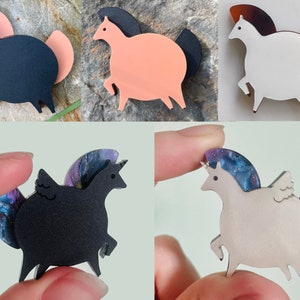 Könnte beinhalten: Drei Holzpferde-Figuren mit verschiedenen Körperfarben und Flügeln. Die erste ist schwarz mit einem rosa Flügel, die zweite ist rosa mit einem schwarzen Flügel und die dritte ist weiß mit einem blauen und violetten Flügel.