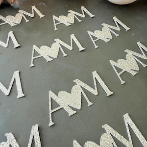 May include: Multiple silver glitter die-cut letter combinations featuring the letter A, a heart shape, and the letter M. Each piece is crafted from a textured, sparkling material and arranged in a scattered pattern across the surface.