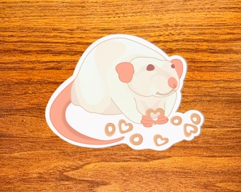 May include: A white rat holding a heart-shaped cookie with other heart-shaped cookies scattered around it.