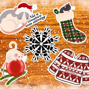 May include: Five Christmas-themed stickers featuring a rat in a stocking, a rat sleeping in a Santa hat, a rat on a Christmas ornament, a snowflake made of rat paw prints, and a red and white sweater with the text "Merry Ratmas" and a rat pattern.