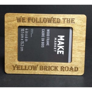 Puede incluir: Un marco de fotos de madera con el texto "We followed the yellow brick road" grabado en la parte delantera. El marco mide 10,1 cm por 15,2 cm y está hecho por Make Market.
