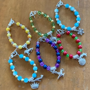 May include: Six beaded bracelets with different colored beads and charms. The charms include a snowflake, a seashell, a genie lamp, a crown, a unicorn, and a shoe.