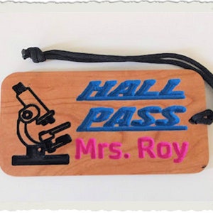 May include: A wooden hall pass with a black microscope image, blue text that says "HALL PASS" and pink text that says "Mrs. Roy".