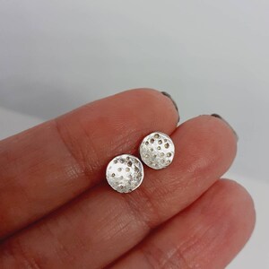 May include: A pair of silver stud earrings with a textured, circular design.