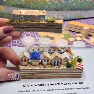 May include: A micro wooden beach hut scene kit. The kit includes miniature beach huts with colorful roofs and striped details, set on a wooden base. The text "Micro wooden beach hut scene kit" is visible.