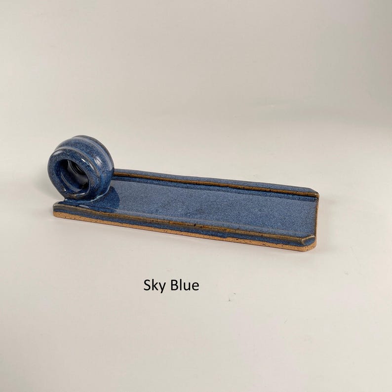 May include: Sky blue ceramic incense holder. The rectangular base has a circular holder at one end. The holder is glazed in sky blue with a brown rim. The text "Sky Blue" is below the holder.