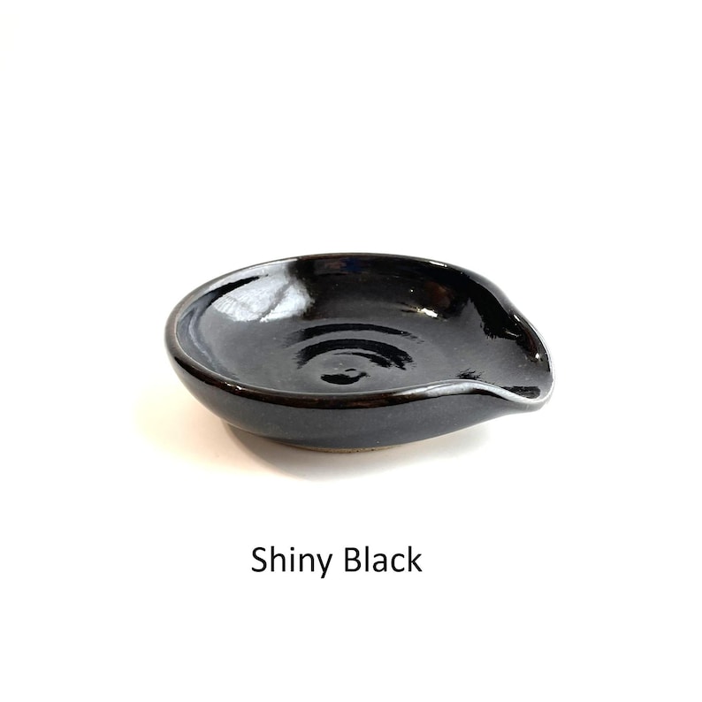 Shiny black glaze, handcrafted spoon rest, shallow round shape with notch for spoon handle, formed on a potter's wheel.