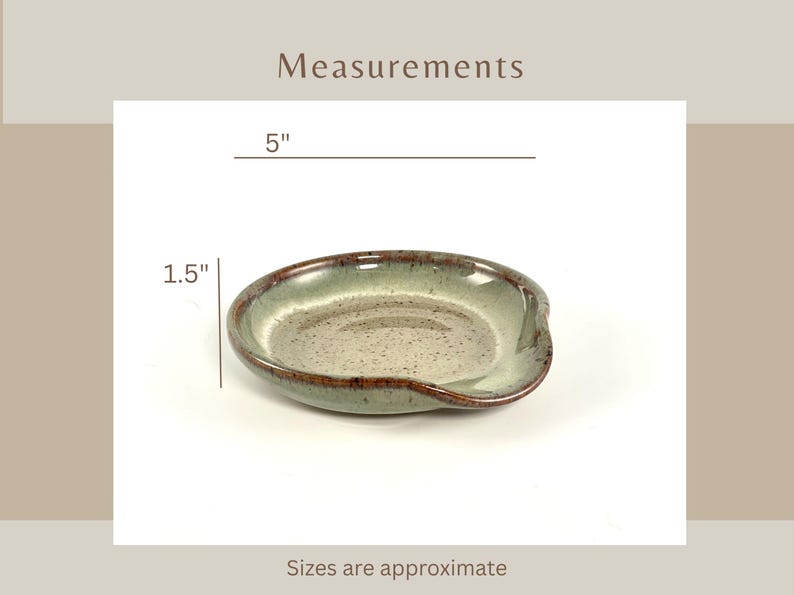 Titled Measurements. A ceramic spoon rest with a speckled gray interior and a green and brown rim. The spoon rest is approximately 5 inches long and 1.5 inches wide. Words on the bottom says sizes are approximate.