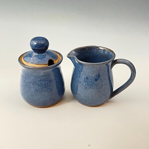 Peut inclure: Un ensemble de pot &agrave; cr&egrave;me et de sucrier en c&eacute;ramique bleue. Le pot &agrave; cr&egrave;me a une poign&eacute;e et le sucrier a un couvercle. Les deux pi&egrave;ces ont un gla&ccedil;age mouchet&eacute;.