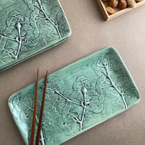 May include: A set of three ceramic mugs with a speckled, matte finish. The mugs are in shades of cream, light gray, and dark gray. Each mug has a simple, modern design and a rounded handle.