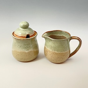 Peut inclure: Un ensemble sucrier et cr&eacute;mier en c&eacute;ramique avec un gla&ccedil;age vert et beige. Le pot &agrave; cr&egrave;me a une poign&eacute;e et le sucrier a un couvercle.