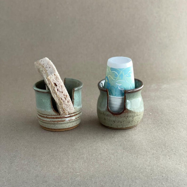 Two Seafoam Green Sponge Holders, the left one is Square Style, holding a drying kitchen sponge. The right Sponge Holder is Belly Style, holding a stack of 3 ounce disposable cups.
