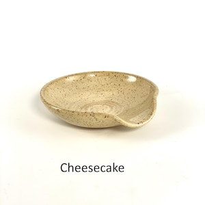Cheesecake glazed handcrafted spoon rest, shallow round shape with notch for spoon handle, formed on a potter's wheel.