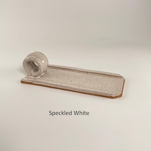 May include: A speckled white ceramic incense holder. It features a rectangular tray with a speckled pattern and a raised edge, and a circular incense holder. The text "Speckled White" is below the holder.