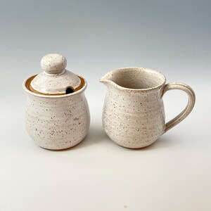 Peut inclure: Ensemble de pot &agrave; cr&egrave;me et sucrier en c&eacute;ramique blanche avec un gla&ccedil;age mouchet&eacute;. Le sucrier a un couvercle avec un bouton.