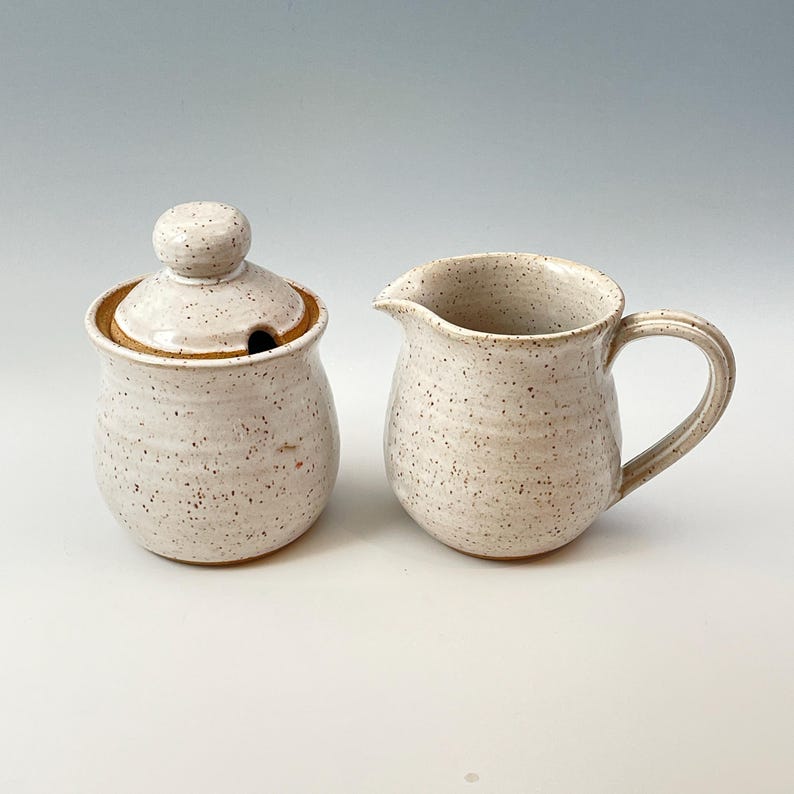 Peut inclure: Ensemble de pot &agrave; cr&egrave;me et sucrier en c&eacute;ramique blanche avec un gla&ccedil;age mouchet&eacute;. Le sucrier a un couvercle avec un bouton.