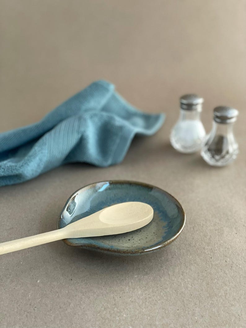 A wooden spoon resting on a Flowing Teal Spoon Rest with salt and pepper shakers next to a cloth