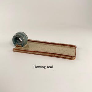 May include: A ceramic incense holder with a flowing teal ring and a rectangular tray. The tray is beige with brown edges. The text "Flowing Teal" is printed below the holder.