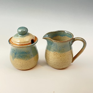 Peut inclure: Un ensemble sucrier et cr&eacute;mier en c&eacute;ramique avec un gla&ccedil;age bleu et beige. Le sucrier a un couvercle avec un bouton sur le dessus. Le cr&eacute;mier a une poign&eacute;e sur le c&ocirc;t&eacute; droit.