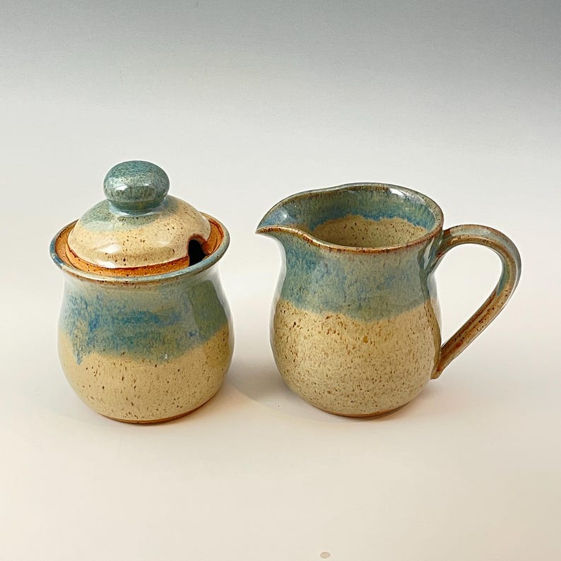 Peut inclure: Un ensemble sucrier et cr&eacute;mier en c&eacute;ramique avec un gla&ccedil;age bleu et beige. Le sucrier a un couvercle avec un bouton sur le dessus. Le cr&eacute;mier a une poign&eacute;e sur le c&ocirc;t&eacute; droit.