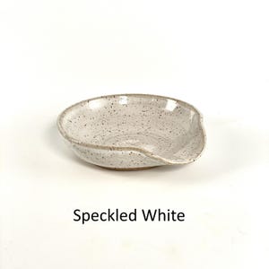 Speckled White glazed, handcrafted spoon rest, shallow round shape with notch for spoon handle, formed on a potter's wheel.