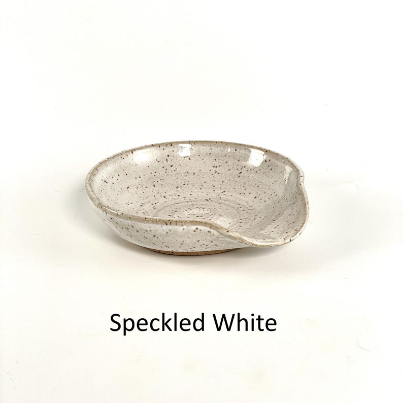 Speckled White glazed, handcrafted spoon rest, shallow round shape with notch for spoon handle, formed on a potter's wheel.