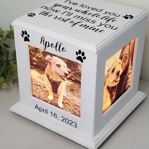 May include: White wooden box with a light inside, featuring two photo slots. The box has a paw print design and the text "I've loved you your whole life now I'll miss you the rest of mine" and "Apollo". The date "April 16, 2023" is also inscribed on the box.