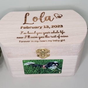 K&ouml;nnte beinhalten: Eine wei&szlig;e Holzkiste mit einem Scharnierdeckel und einem Messingverschluss. Die Kiste hat ein Foto eines Hundes auf der Vorderseite und ist mit dem Text "Lola", "13. Februar 2023", "Ich habe dich dein ganzes Leben lang geliebt, jetzt werde ich dich f&uuml;r den Rest meines Lebens vermissen" und "F&uuml;r immer in meinem Herzen mein kleines M&auml;dchen" graviert.