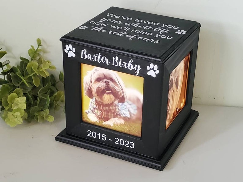 Może przedstawiać: Czarne drewniane pudełko na zdjęcia z obrazkiem psa w środku. Pudełko ma odciski łap i napis "We've loved you your whole life now we'll miss you the rest of ours" na g&oacute;rze. Pudełko ma r&oacute;wnież napis "Baxter Bixby" i "2015-2023" z przodu.