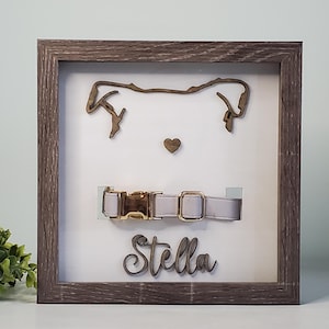 May include: A wooden frame with a white background, featuring a cutout of a dog's head, a pink collar with a gold buckle, and the name "Stella" written in cursive.