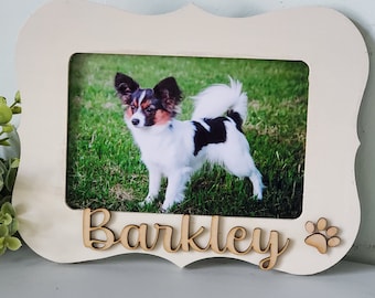May include: White wooden picture frame with a scalloped edge. The frame has a photo of a small black and white dog with brown ears. The dog's name, "Barkley", is written in cursive on the frame, along with a paw print.