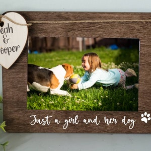 May include: A brown wooden photo frame with a white heart-shaped tag that says "Leah & Cooper". The frame has a photo of a girl and a dog playing in a grassy field. The text "Just a girl and her dog" is written below the photo with a paw print.