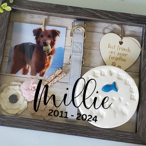 May include: A framed pet memorial with a photo of a dog holding a ball, a collar, and a paw print. The frame includes the name "Millie" and the years "2011-2024". Decorative flowers and a heart-shaped wooden tag are also included.