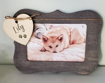May include: A gray wooden picture frame with a heart-shaped wooden tag that says "Lily" with paw prints. The frame holds a photo of a white dog lying on a bed.