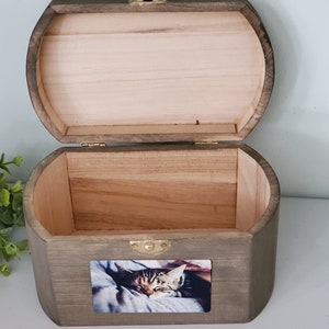 K&ouml;nnte beinhalten: Eine Holzkiste mit einem Scharnierdeckel, in einem dunklen Braunton gebeizt. Die Kiste hat ein kleines Foto eines schlafenden Katers auf der Vorderseite.
