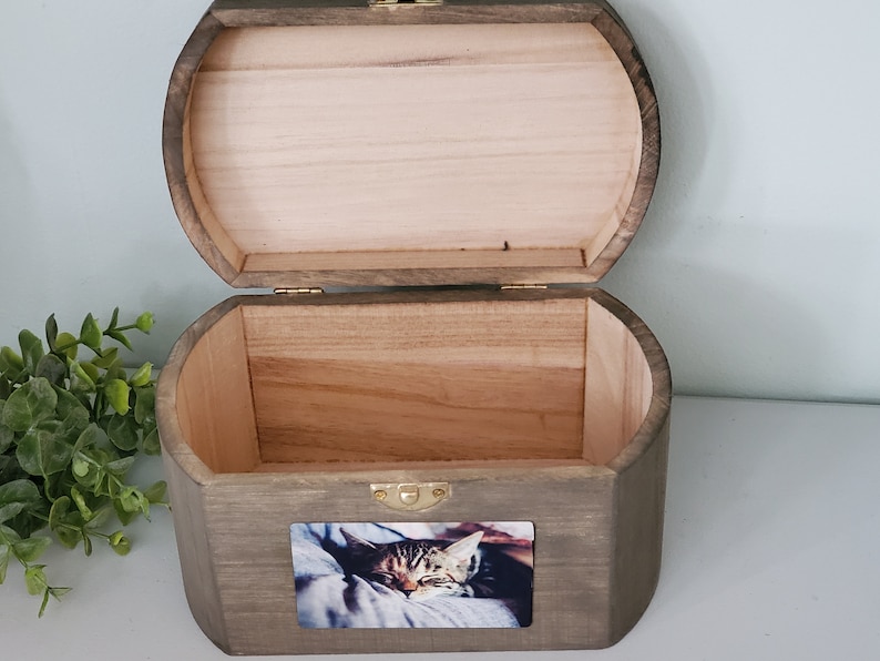 K&ouml;nnte beinhalten: Eine Holzkiste mit einem Scharnierdeckel, in einem dunklen Braunton gebeizt. Die Kiste hat ein kleines Foto eines schlafenden Katers auf der Vorderseite.