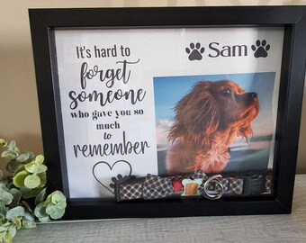 May include: A black shadow box memorial frame with a photo of a dog, a dog collar, and a dog tag. The frame has a white background with the text "It's hard to forget someone who gave you so much to remember." and the name "Sam" with paw prints.
