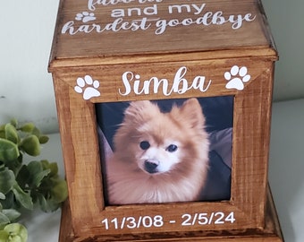 Puede incluir: Una caja de madera con un marco de fotos y un diseño de huella de pata. El marco contiene una foto de un perro pequeño de color marrón claro. La caja tiene el texto "You were my favorite hello and my hardest goodbye" y "Simba". Las fechas "11/3/08 - 2/5/24" también están en la caja.