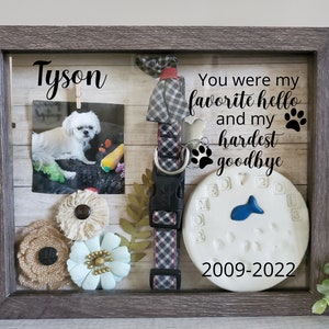 May include: A framed memorial for a dog named Tyson. The frame includes a photo of the dog, a collar, flowers, and a paw print with the dates 2009-2022. The text reads "You were my favorite hello and my hardest goodbye".