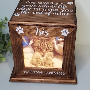 Może przedstawiać: Drewniana skrzynka z fotografią kota w środku. Skrzynka ma biały napis: "I've loved you your whole life now I'll miss you the rest of mine." Nazwa kota, "Isis", jest napisana pod zdjęciem. Daty "11/25/2004 - 03/07/2023" są wygrawerowane pod nazwą.