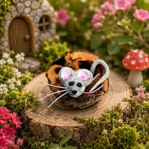 May include: A small, glittery silver mouse figurine with pink-tinted ears, black bead eyes, a black nose, and long white whiskers. The mouse has a curved tail and is positioned inside a dark, textured wooden hollow on a round tree stump.