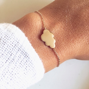 May include: A gold chain bracelet with a cloud charm. The bracelet is on a person's wrist.