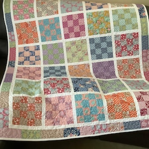 May include: A patchwork quilt with a white background and squares of various floral patterns in shades of pink, blue, green, and red.