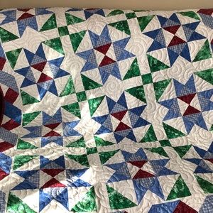 May include: A quilt with a patchwork design featuring blue, green, and red stars on a white background. The quilt is quilted with a swirling pattern.